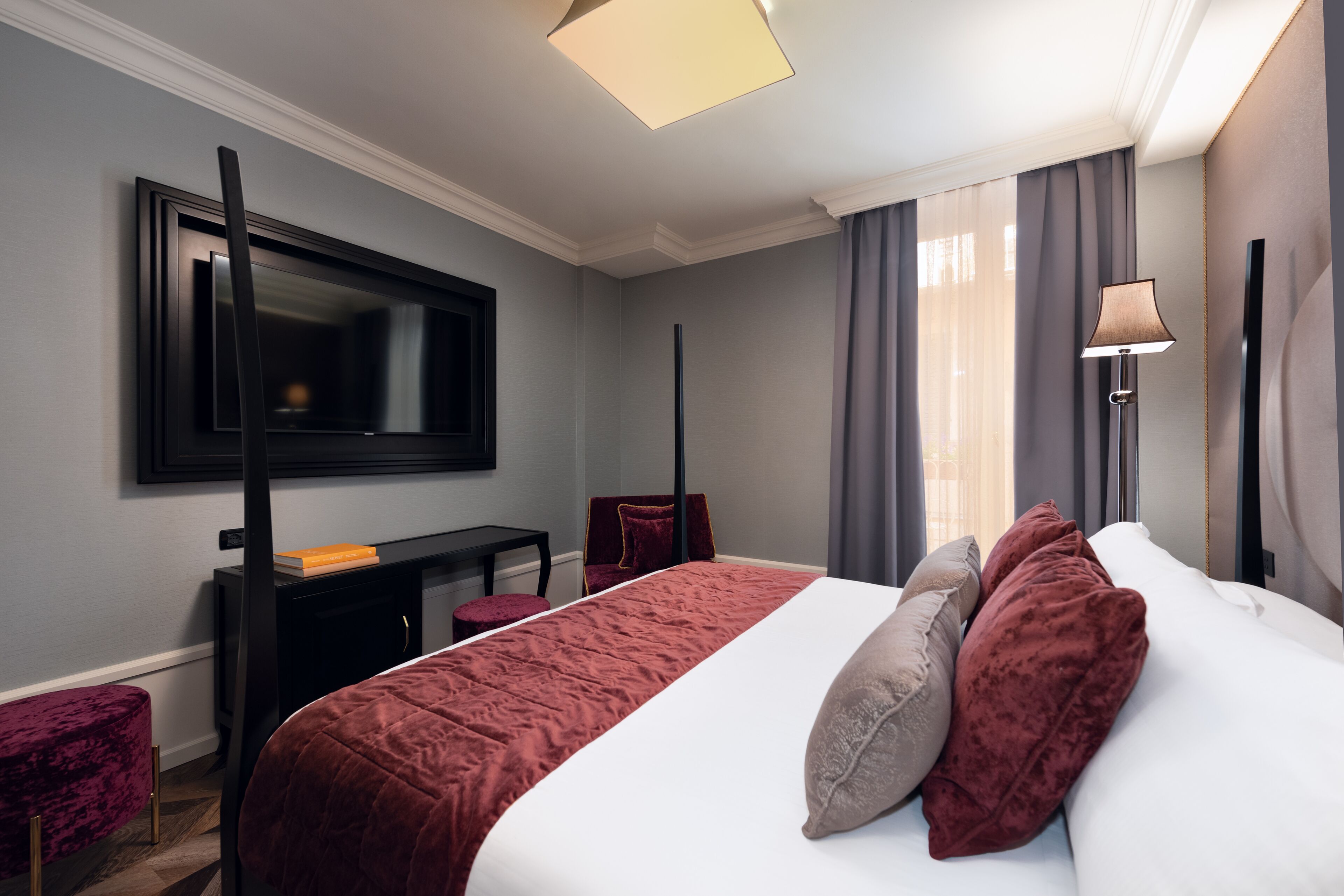 A hotel room with a large bed, a desk, a chair, a TV, and a lamp.