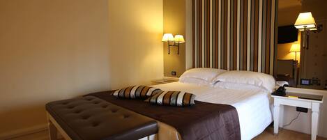 A hotel room with a bed, a bedside table, a lamp, and a TV.