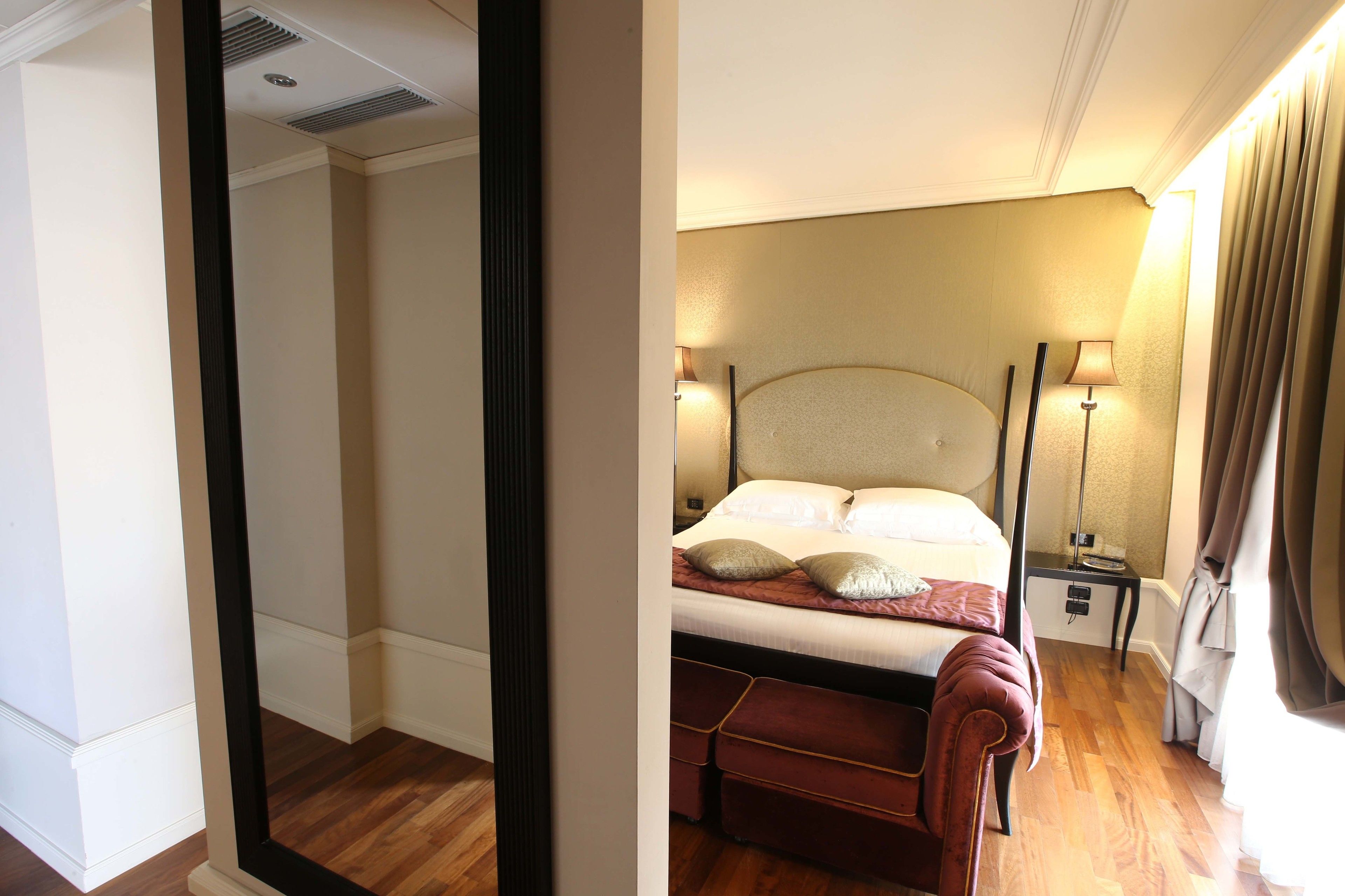 A hotel room with a bed, bedside lamps, a nightstand, and a mirror.