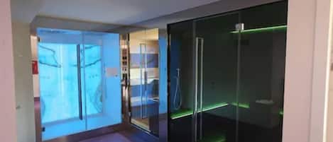 A modern hotel corridor with glass doors leading to a room, a visible shower area, and a green-lit wall.
