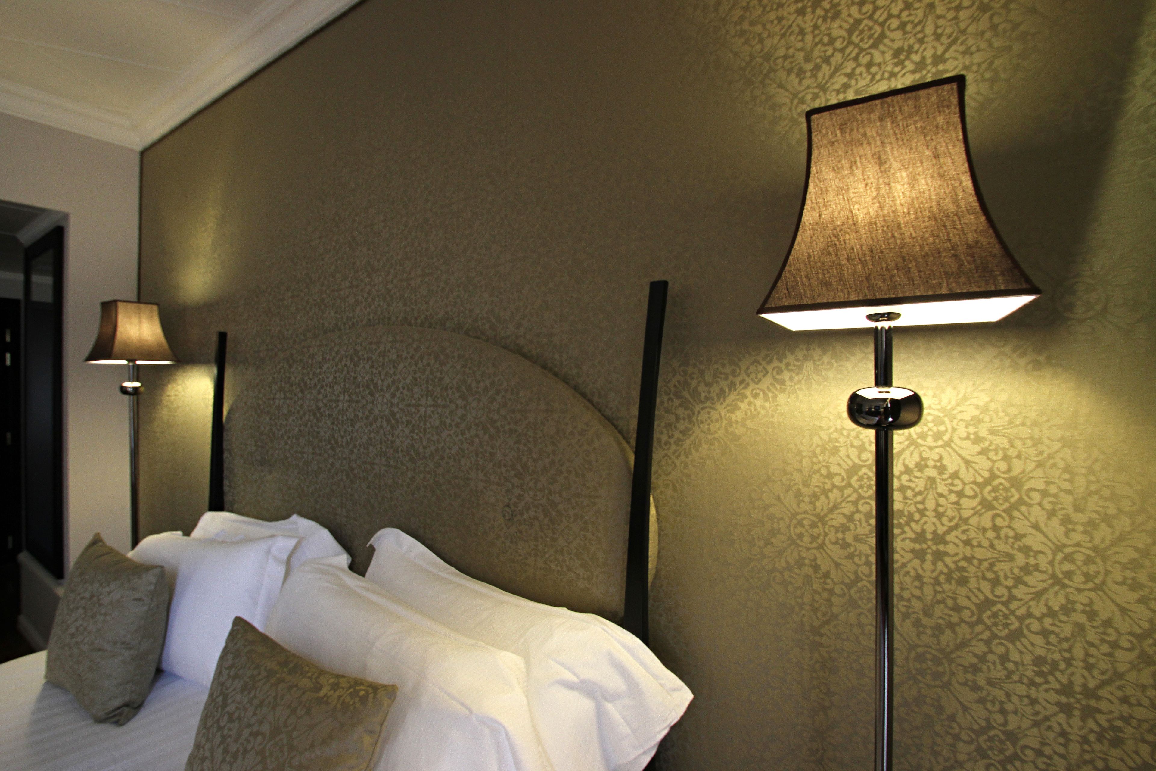 A hotel room with a neatly made bed, two bedside lamps, and a patterned wallpaper.