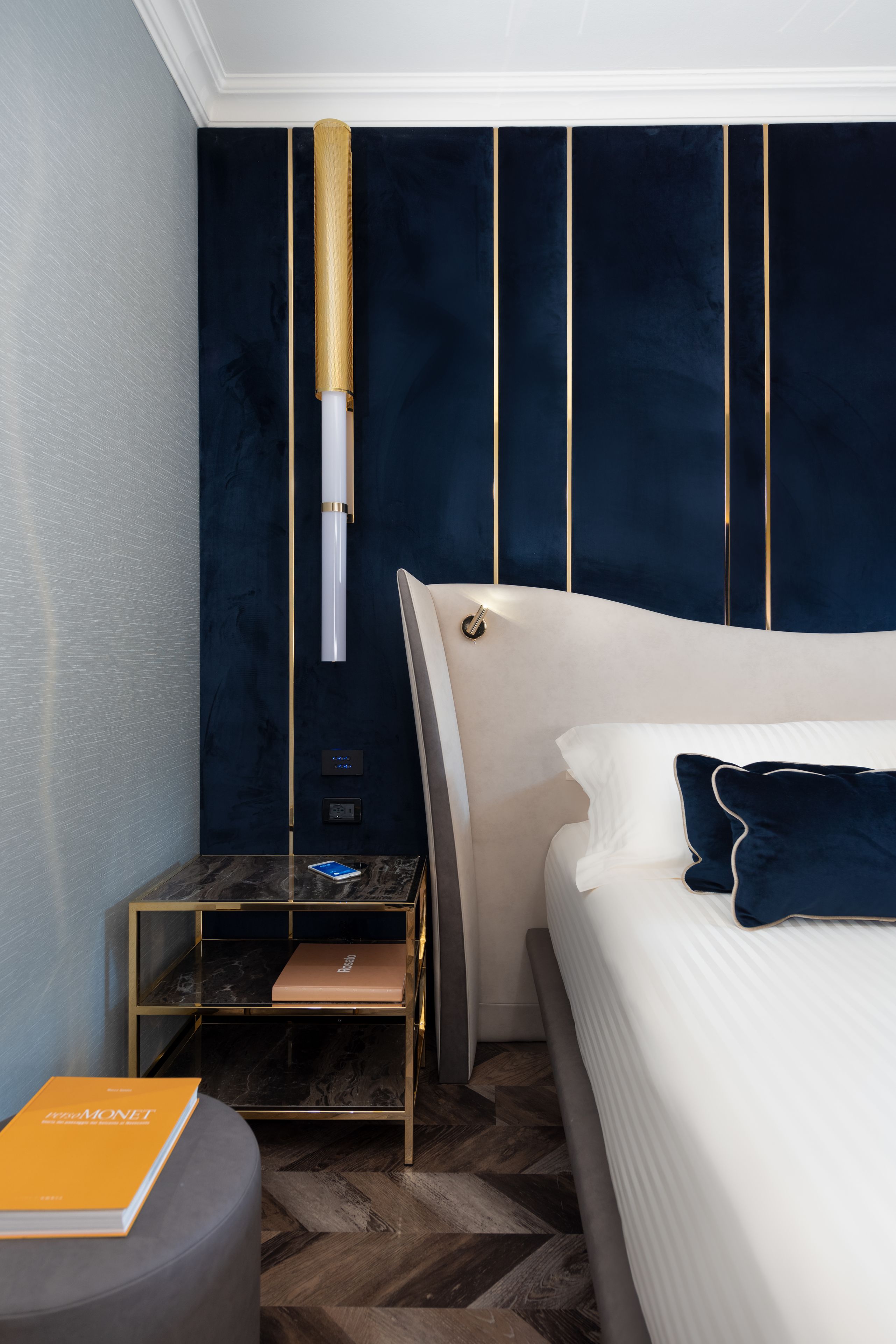 Moderni hotellihuone, jossa on suuri sänky, yöpöytä, yövalaisin ja seinään kiinnitetty valaisin.