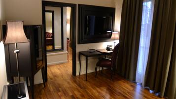 A hotel room with a wooden floor, a desk with a chair, a television, and a lamp.