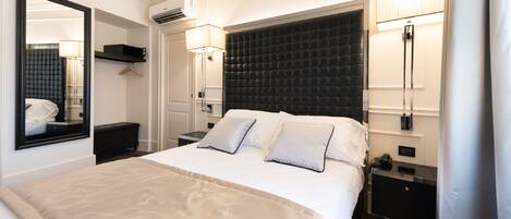 Una habitación de hotel moderna con una cama grande, un cabecero oscuro, lámparas de noche, un espejo, una mesita de noche y un equipo de aire acondicionado.