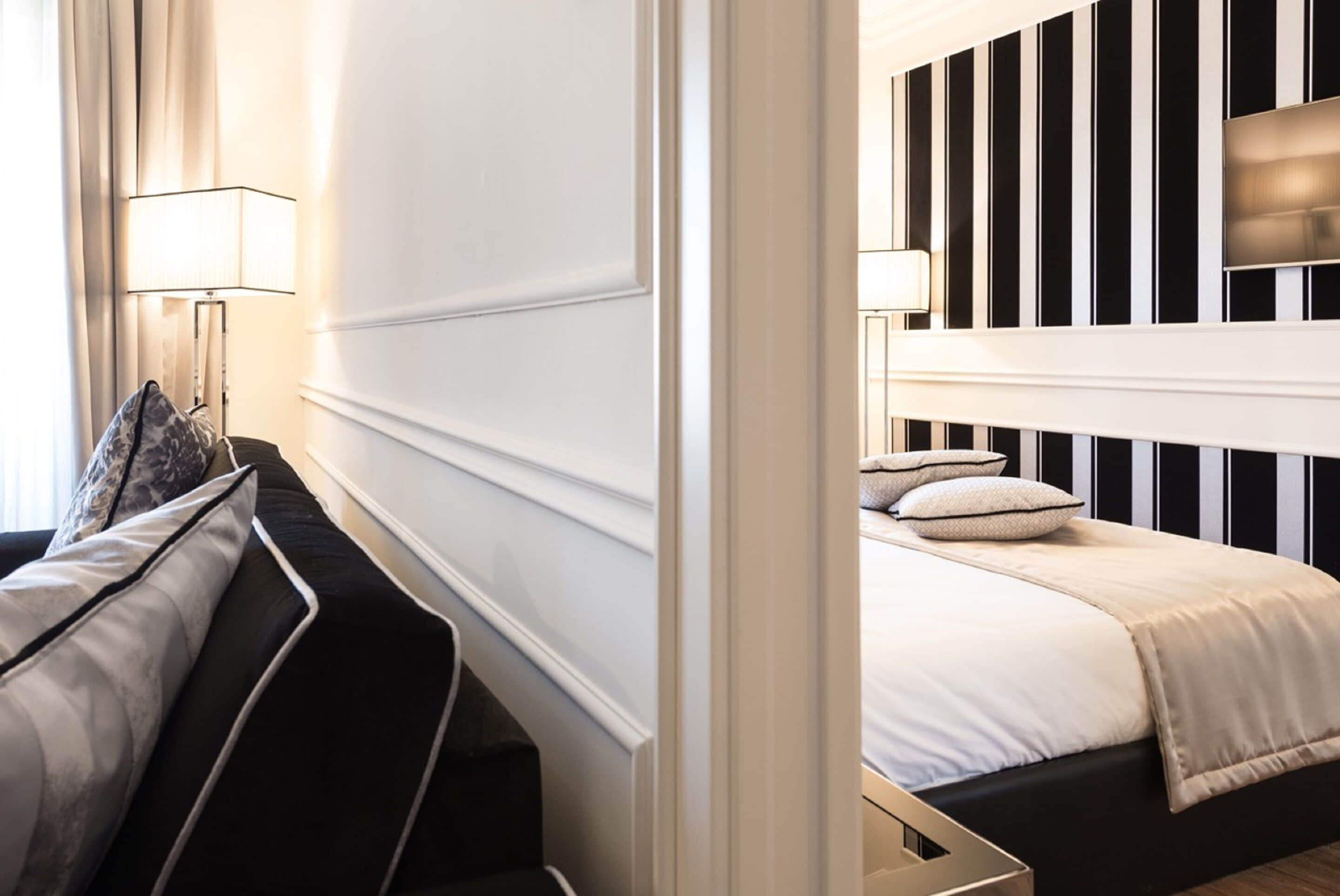 A hotel room with a bed, a nightstand with a lamp, and a sofa with cushions.