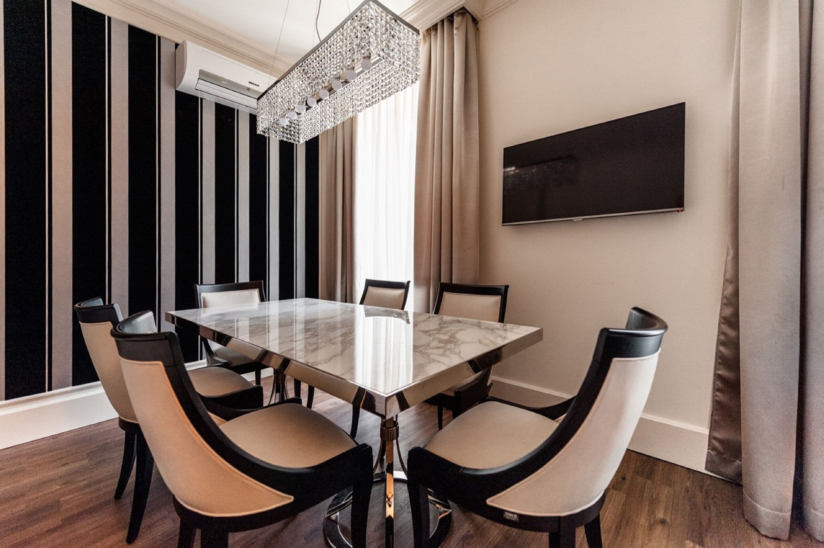 A modern dining room with a marble table, six chairs, a chandelier, and a large painting on the wall.