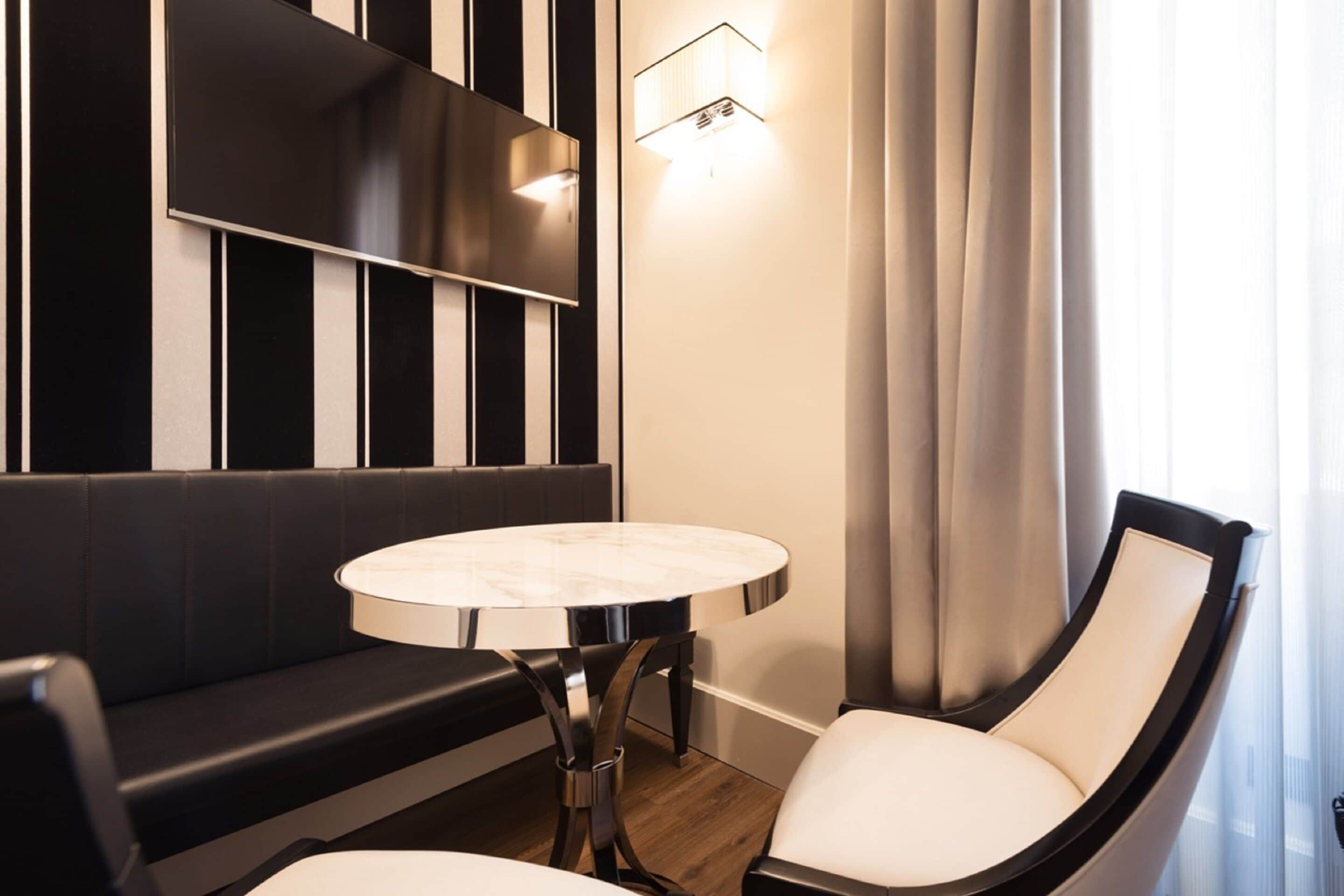 Ein modernes Hotelzimmer mit einer schwarz-weiß gestreiften Wand, einem runden Marmortisch, einem weißen Sitzsessel und einem schwarzen Sofa.
