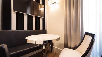 Ein modernes Hotelzimmer mit einer schwarz-weiß gestreiften Wand, einem runden Marmortisch, einem weißen Sitzsessel und einem schwarzen Sofa.