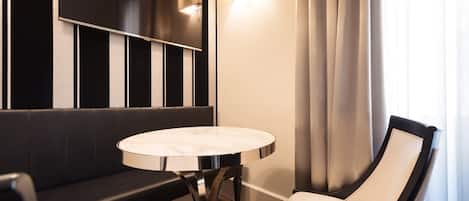 Una habitación de hotel moderna con una pared a rayas blancas y negras, una mesa redonda de mármol, una silla blanca acolchada y un sofá negro.