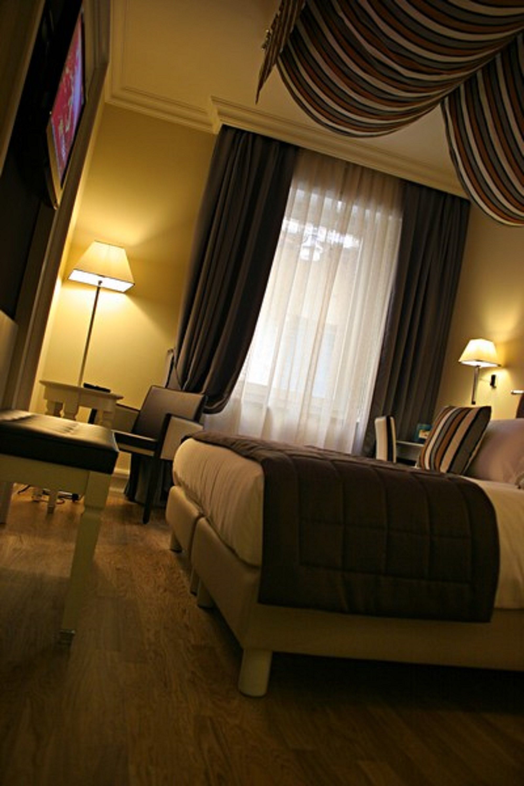 Una habitación de hotel con cama, escritorio, silla, lámpara y cortinas.