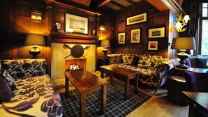 A cozy room with a fireplace, patterned sofas, and wooden walls. - Savoy Park Hotel (Ayr)