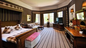 A hotel room with a large bed, a sofa, a TV, a desk with a mirror, and a view of greenery outside. - Savoy Park Hotel (Ayr)