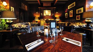 A restaurant with a wooden table set for dining, a sofa with a patterned cushion, and wall-mounted picture frames. - Savoy Park Hotel (Ayr)