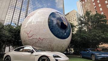 A modern building with a glass facade, a large spherical sculpture, and a sports car parked on a grassy area.