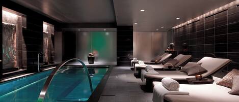 Un área de piscina interior moderna con sillones de descanso y una piscina cristalina.