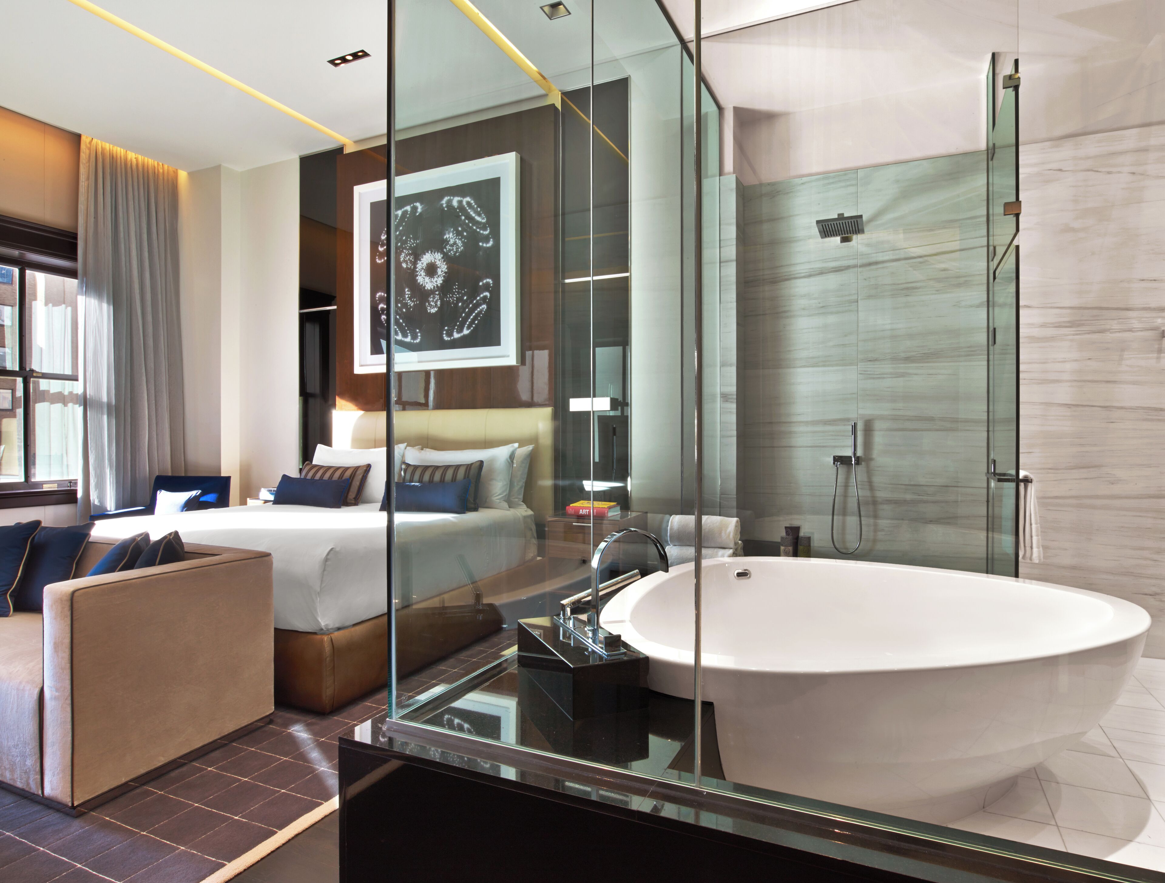 Una habitación de hotel moderna con una cama grande, un baño con paredes de vidrio y una bañera espaciosa.