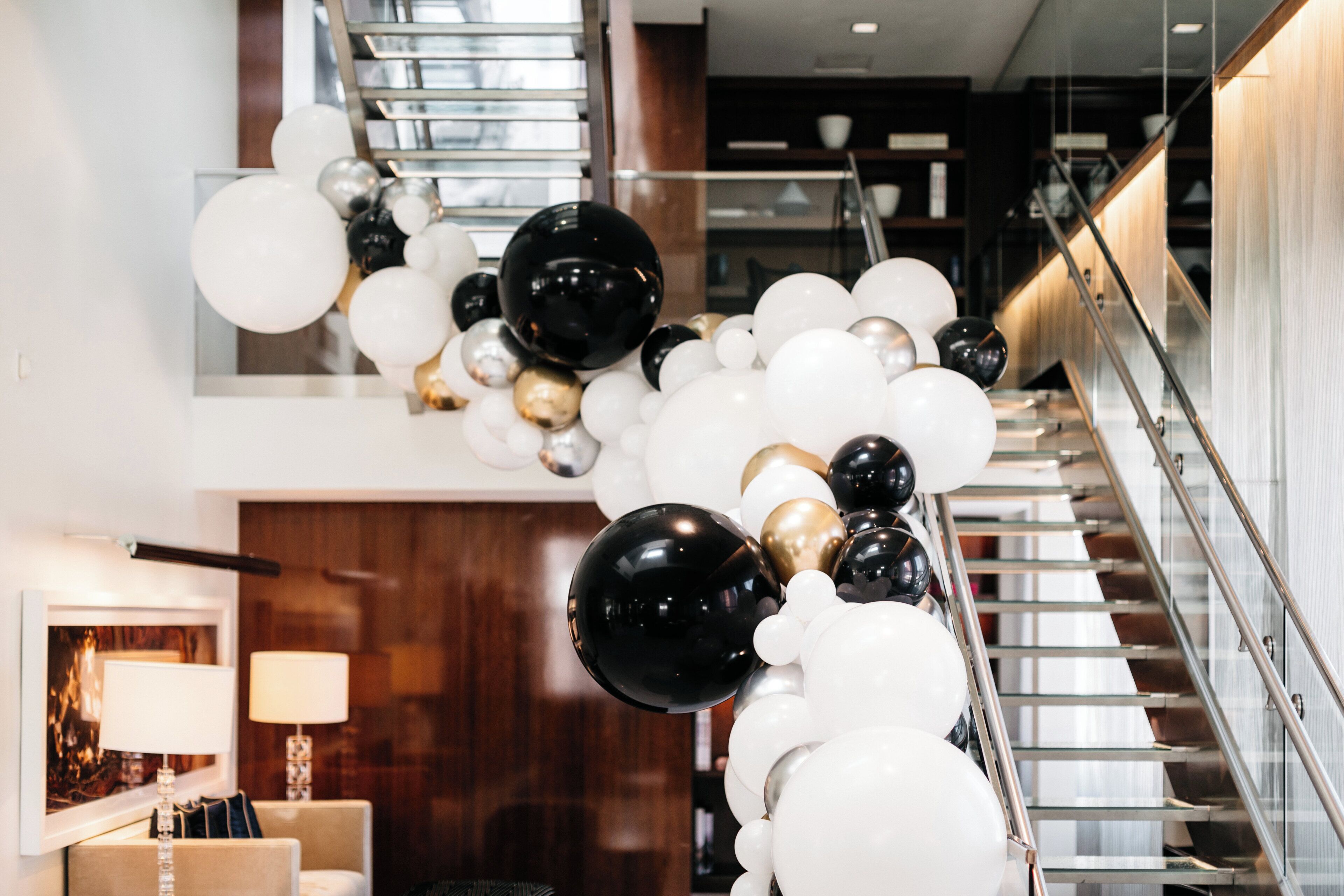 A staircase with a modern design, surrounded by a decorative arrangement of white, black, and gold balloons.