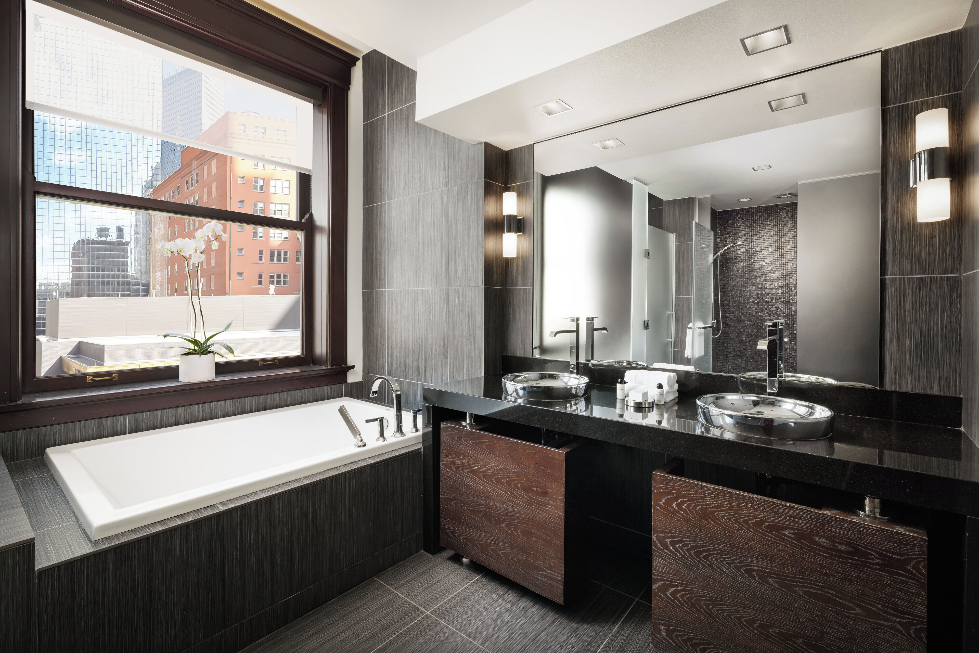 A modern bathroom with a large window, dual sinks, and a vanity with wooden drawers.