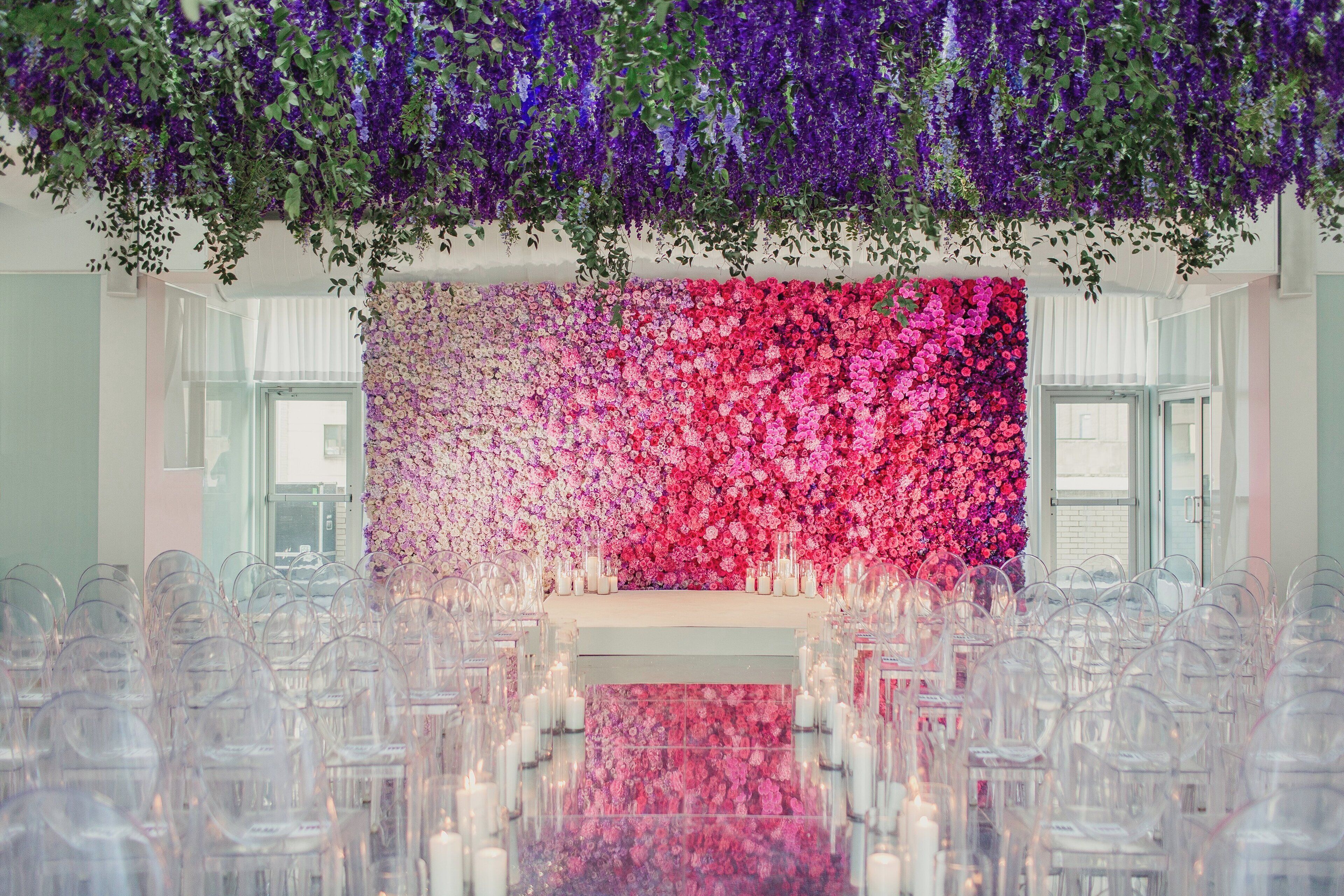 A venue with a floral backdrop, clear chairs, and a reflective floor.