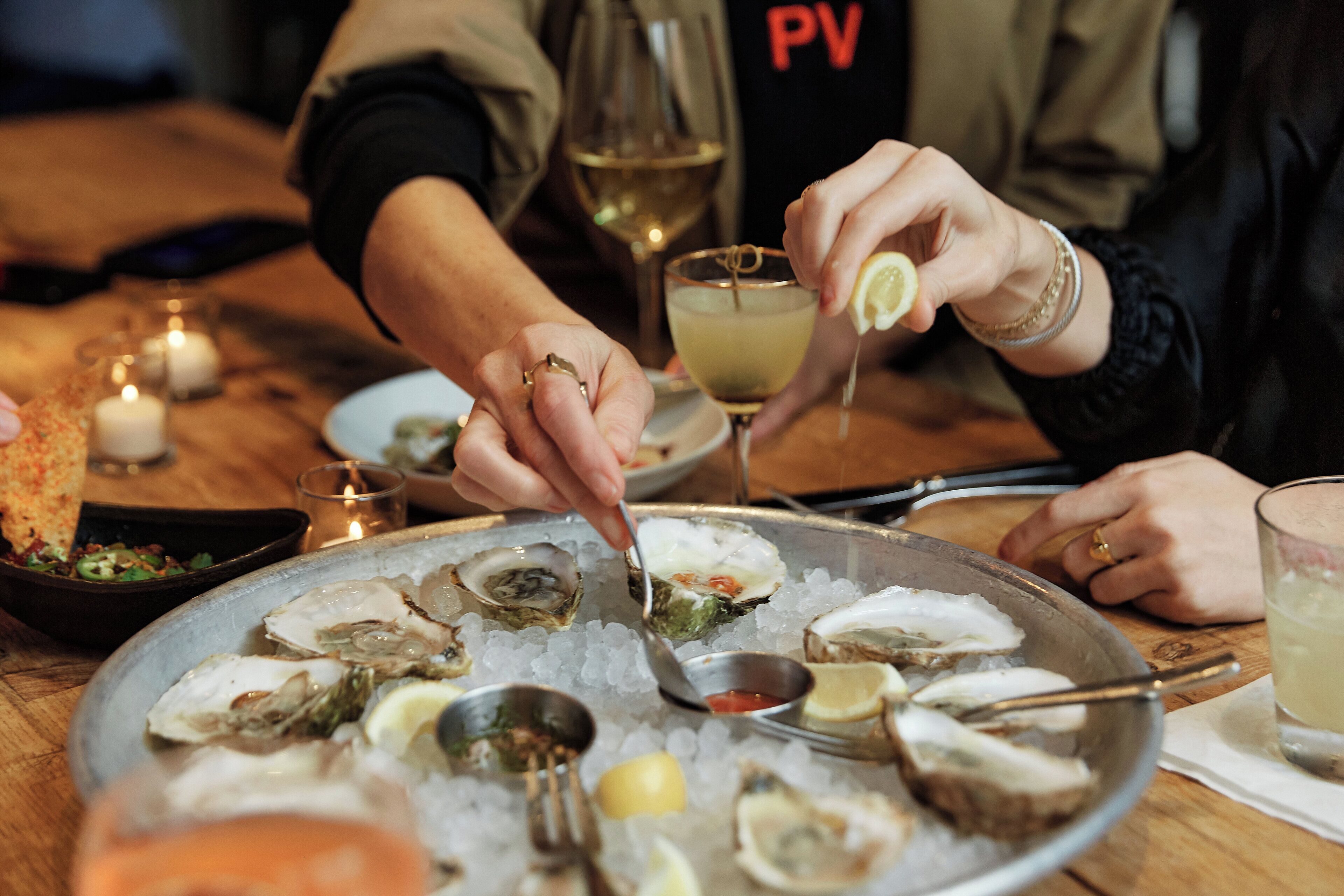 A dining table with oysters on ice, a glass of white wine, and a candle.