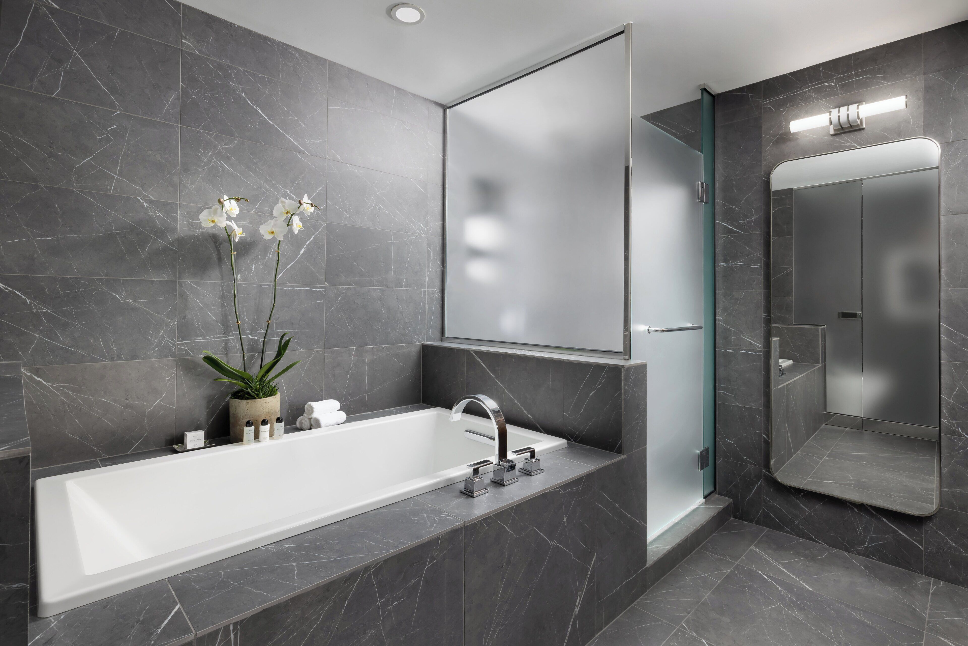 Une salle de bain moderne avec une grande baignoire, une douche en verre et un mur recouvert de carreaux de marbre.