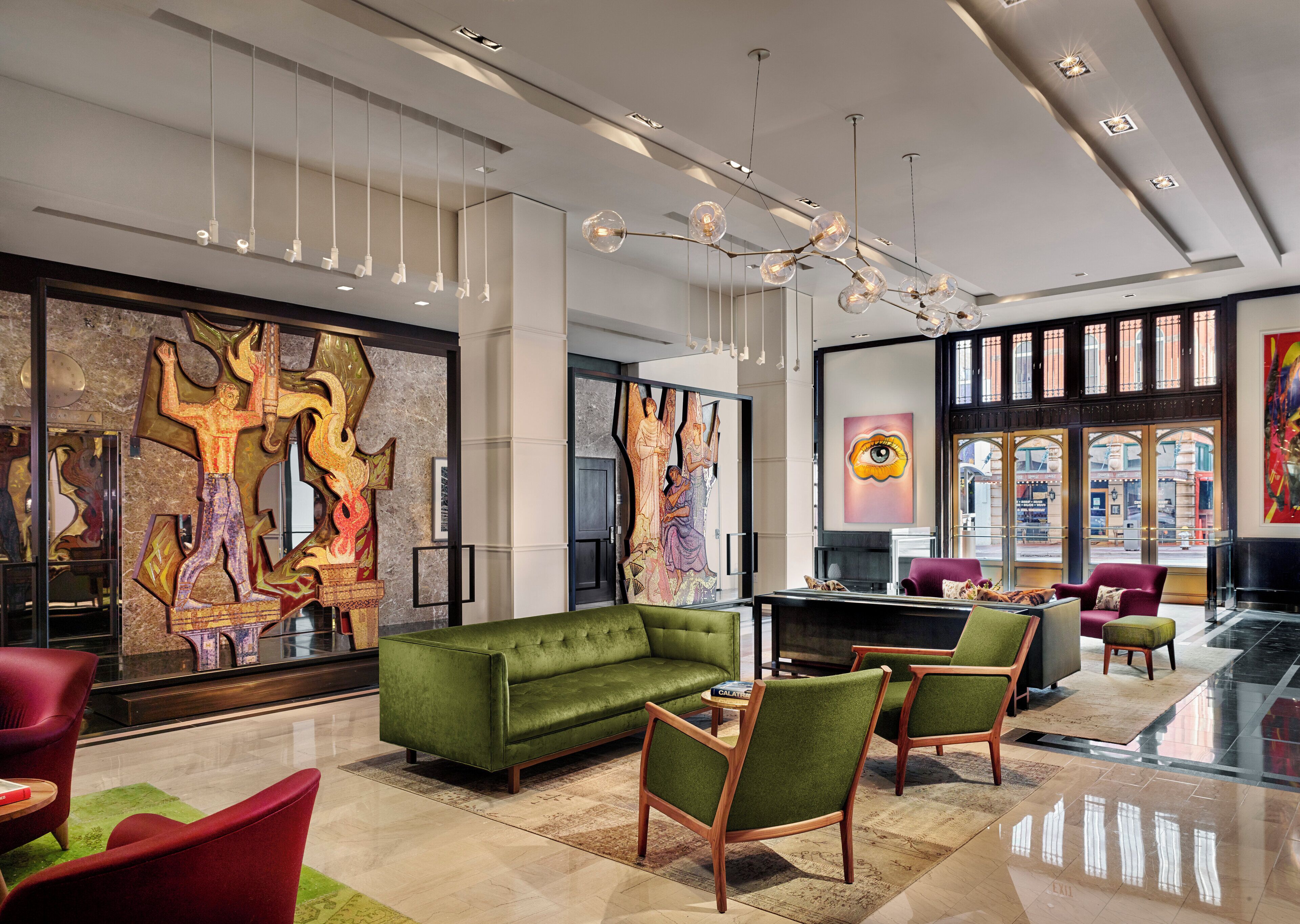 Eine großzügige Lobby mit einem grünen Sofa, roten Sesseln und einem großen abstrakten Gemälde.