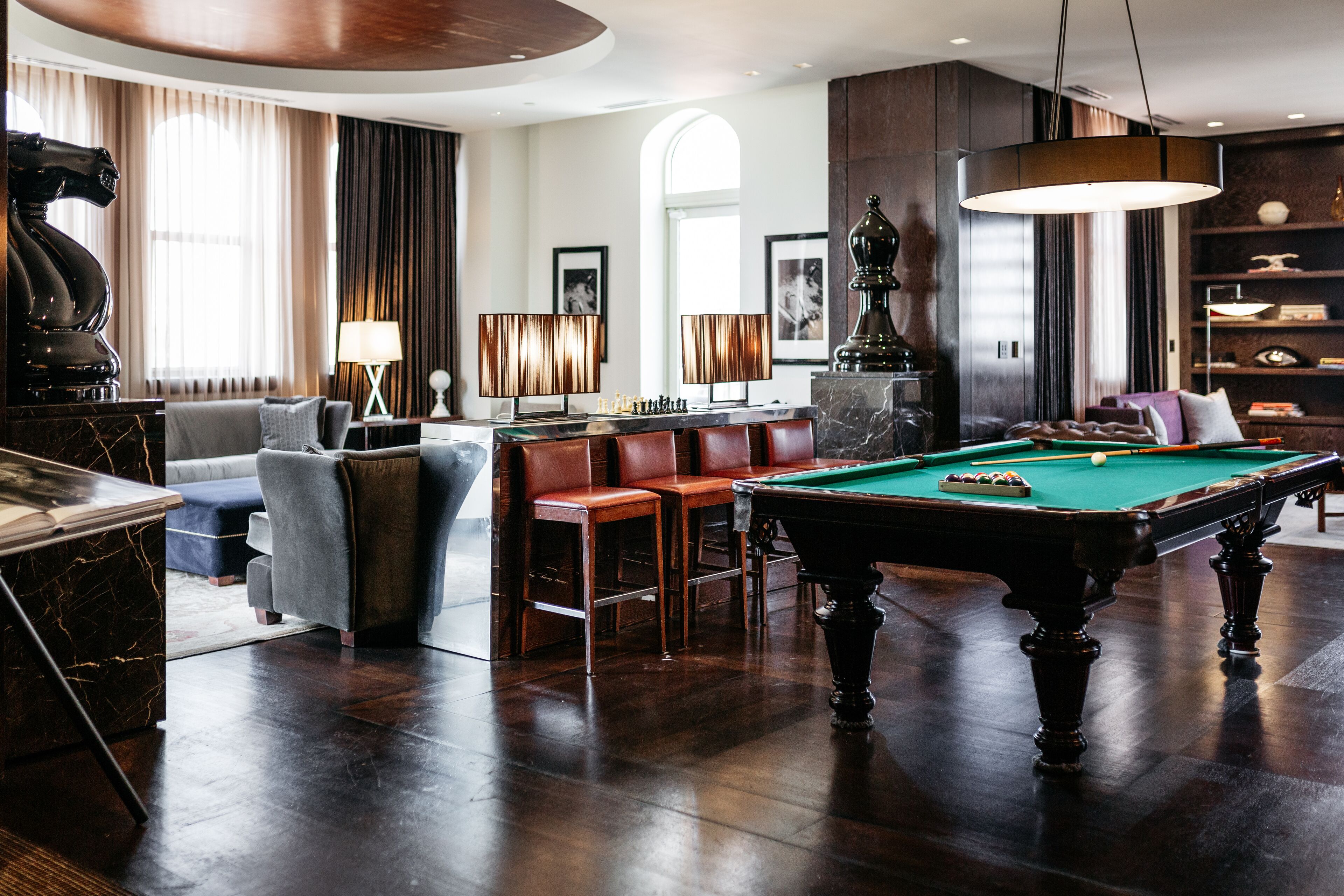 Una habitación bien iluminada con mesa de billar, sillones de cuero, sofá y zona de bar.