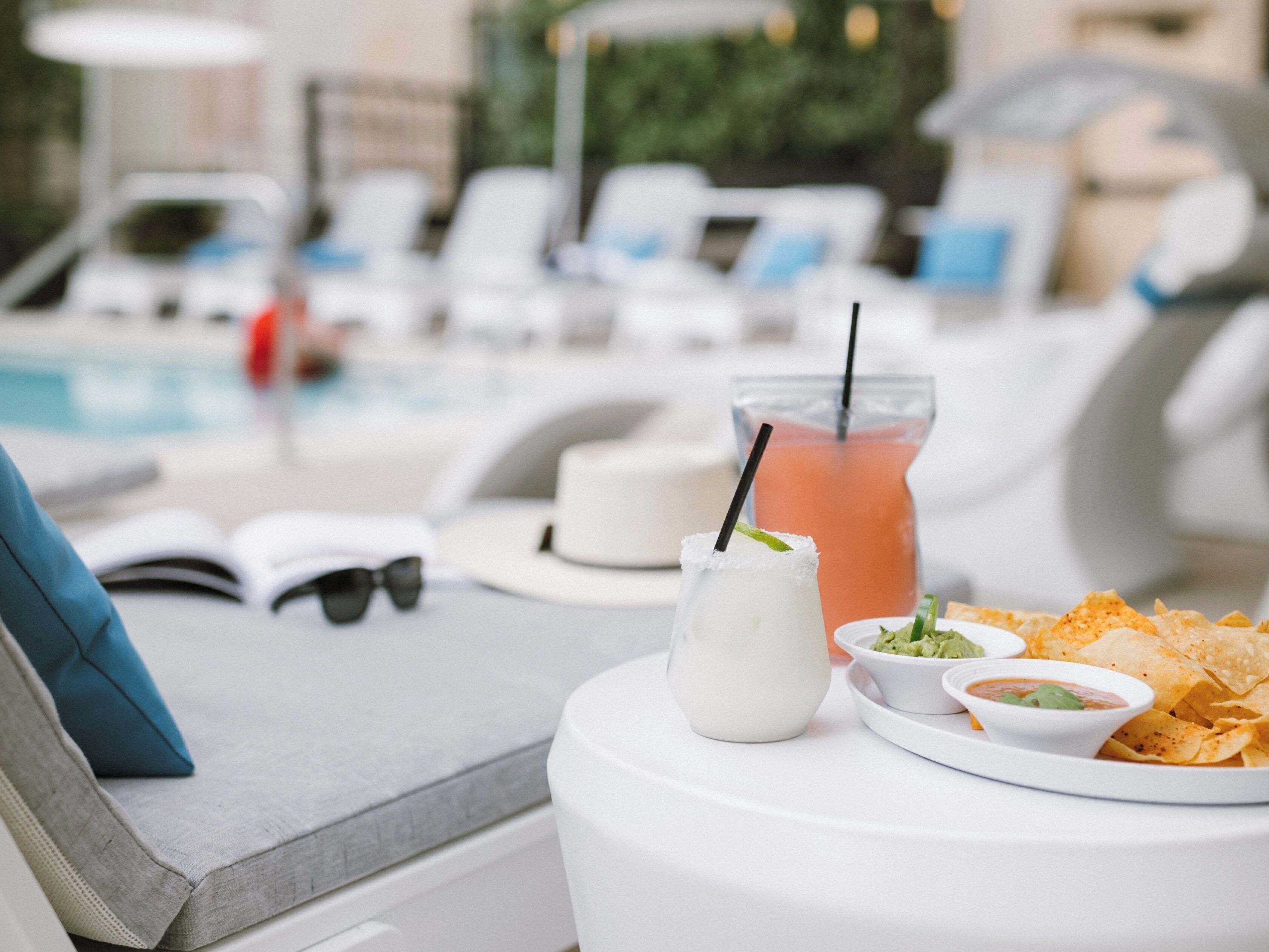 Un área de descanso junto a la piscina con una mesa blanca, té helado, una margarita, totopos y salsa.