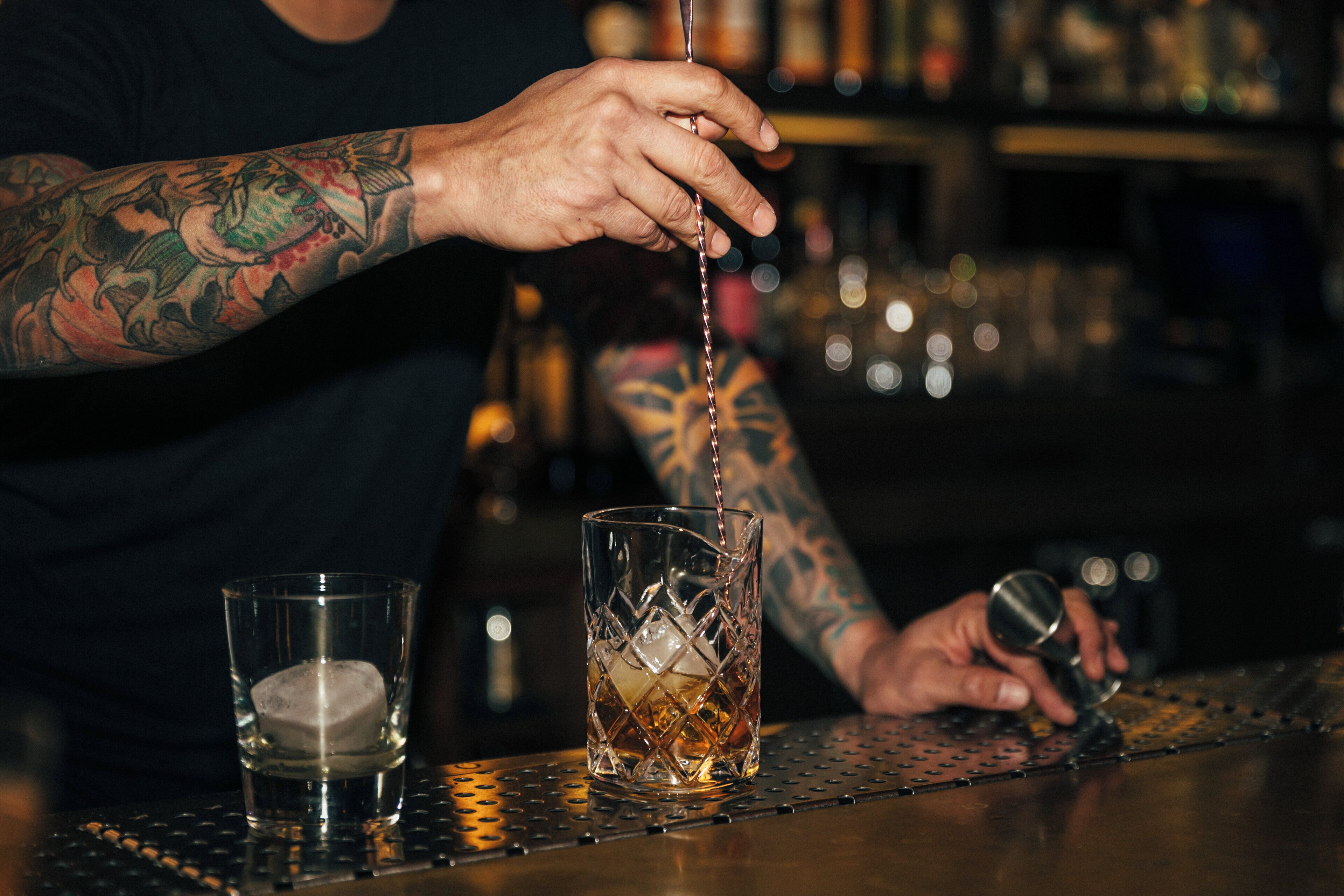 A bartender pouring a drink into a glass with ice cubes.