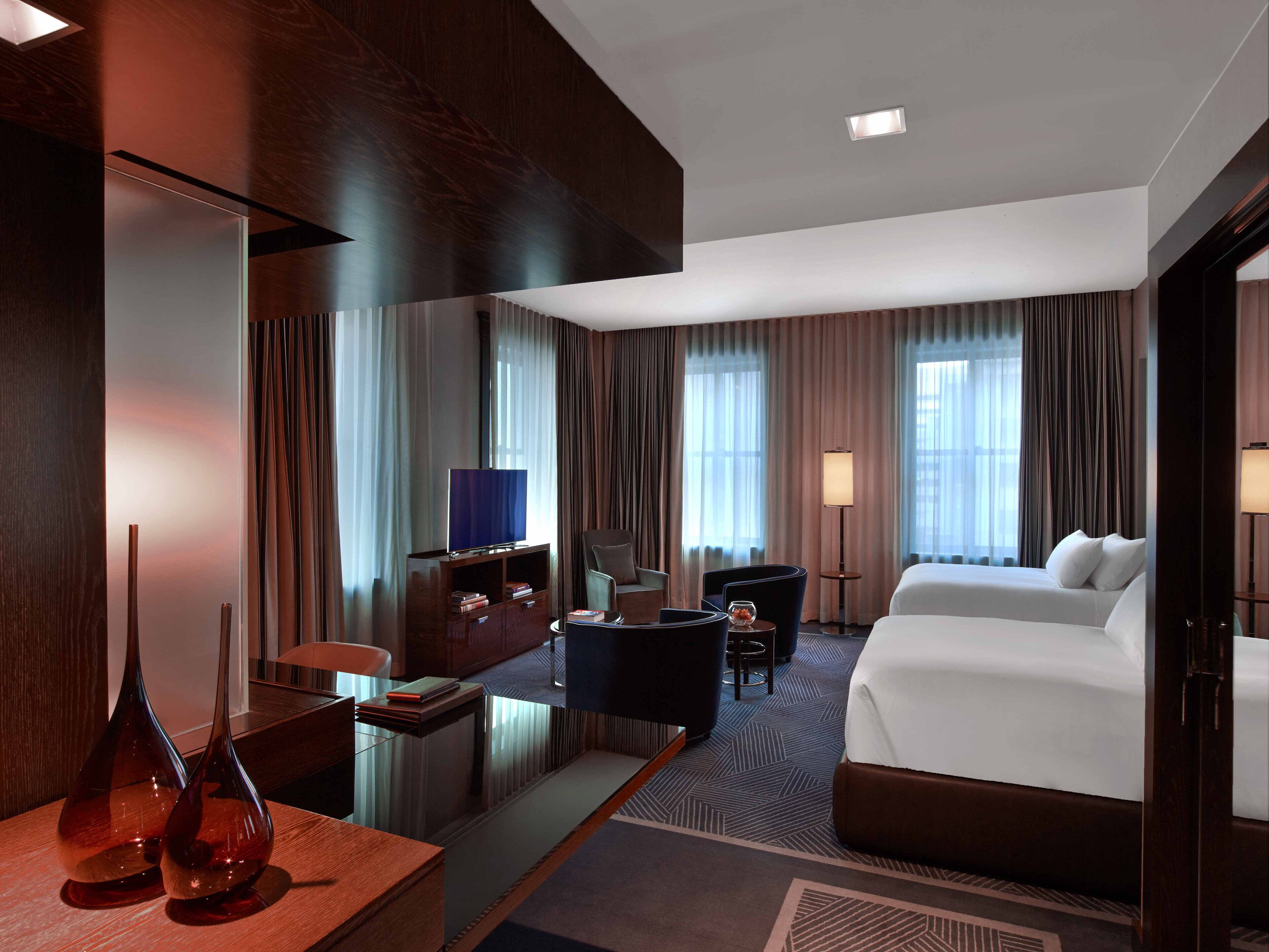 Habitación de hotel con cama, escritorio, computadora, silla, televisor y lámpara.