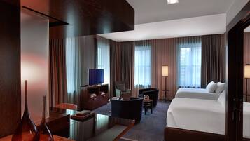 Habitación de hotel con cama, escritorio, computadora, silla, televisor y lámpara.