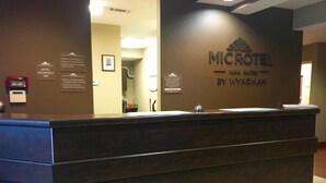 A reception desk at the Microtel Inn Suites by Wyndham with a brown counter, a framed picture on the wall, and a sign indicating hotel occupancy.