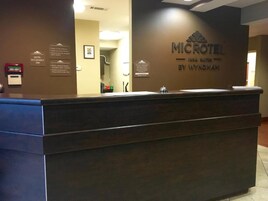 Mostrador de recepción del Microtel Inn Suites by Wyndham, con una barra marrón, un cuadro en la pared y un cartel que indica la ocupación del hotel.