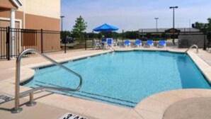A swimming pool with a metal ladder, blue lounge chairs, and a blue umbrella.