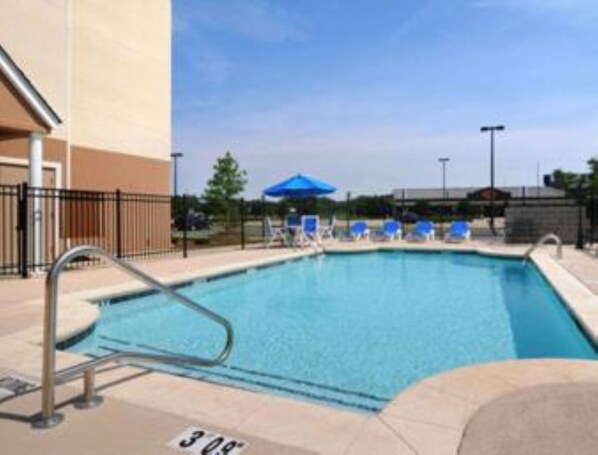 A swimming pool with a metal ladder, blue lounge chairs, and a blue umbrella.