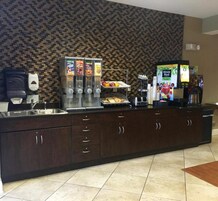 Una cocina con un mueble de madera oscura, una cafetera, una exposición de frutas y un refrigerador.