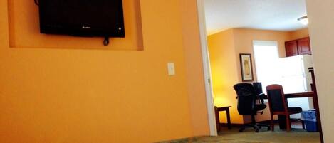A hotel room with a bed, a television mounted on the wall, a desk with a chair, and a window.