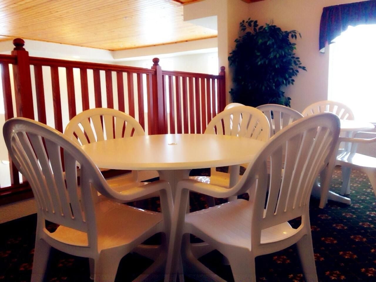 A round table with four white plastic chairs in a room with a wooden ceiling and a red railing.