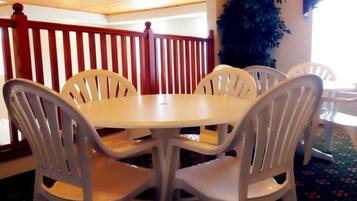 A round table with four white plastic chairs in a room with a wooden ceiling and a red railing.