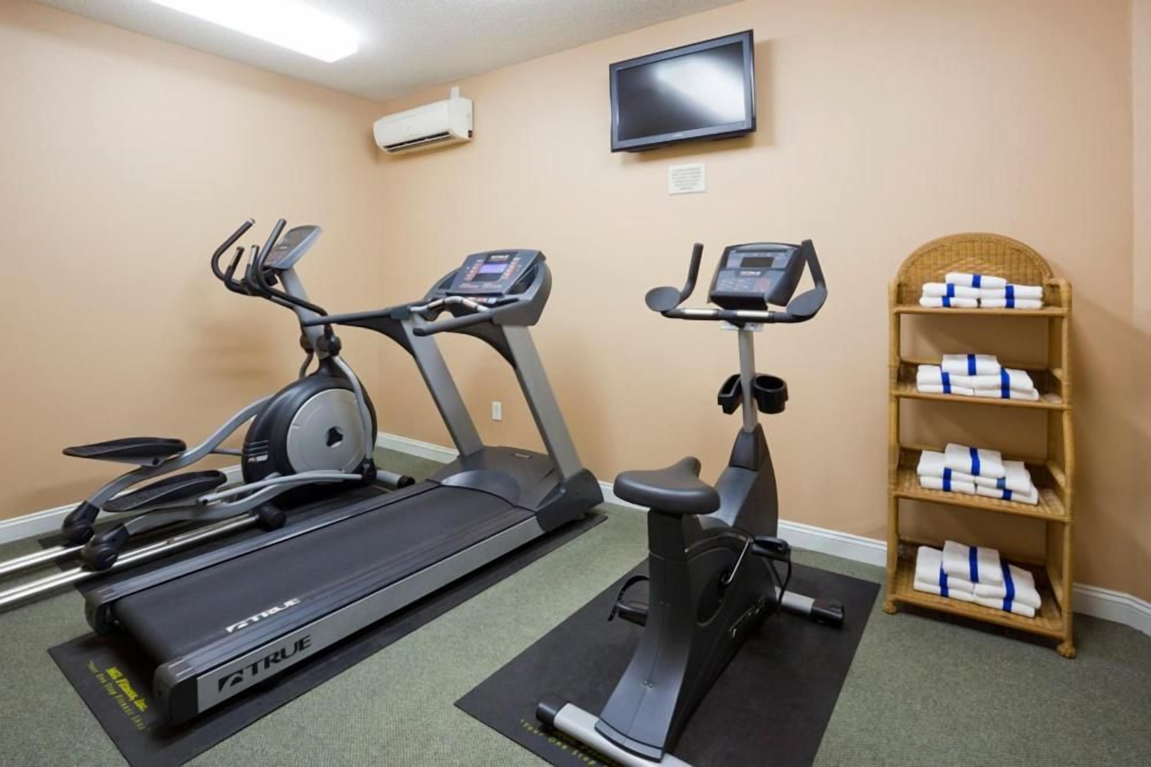 A fitness room with two treadmills, a stationary bike, a television on the wall, and a shelf with towels.