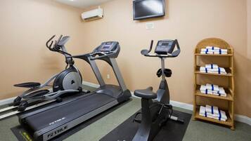 A fitness room with two treadmills, a stationary bike, a television on the wall, and a shelf with towels.