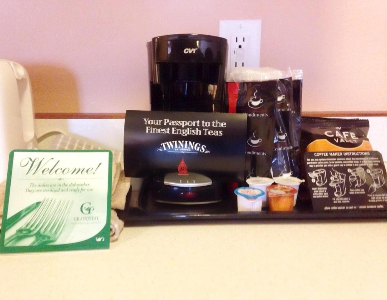 Tarjottimella on kahvinkeitin, Twinings-teepusseja, kahvinkeittimen käyttöohje ja tervetulokyltti.
