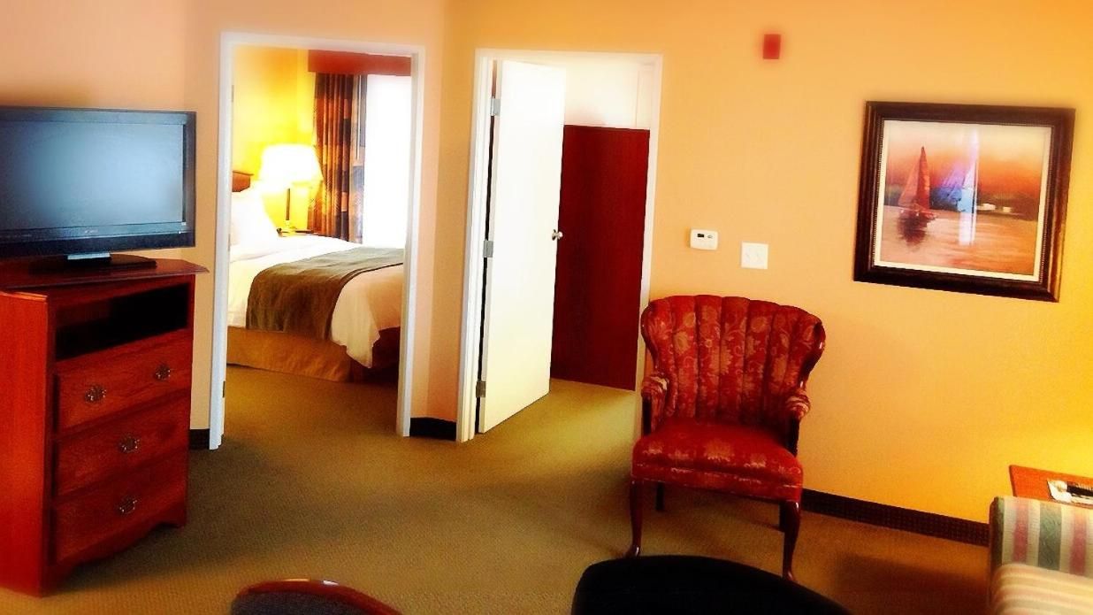 Una habitación de hotel con una televisión, un sillón rojo, una cama y un cuadro en la pared.