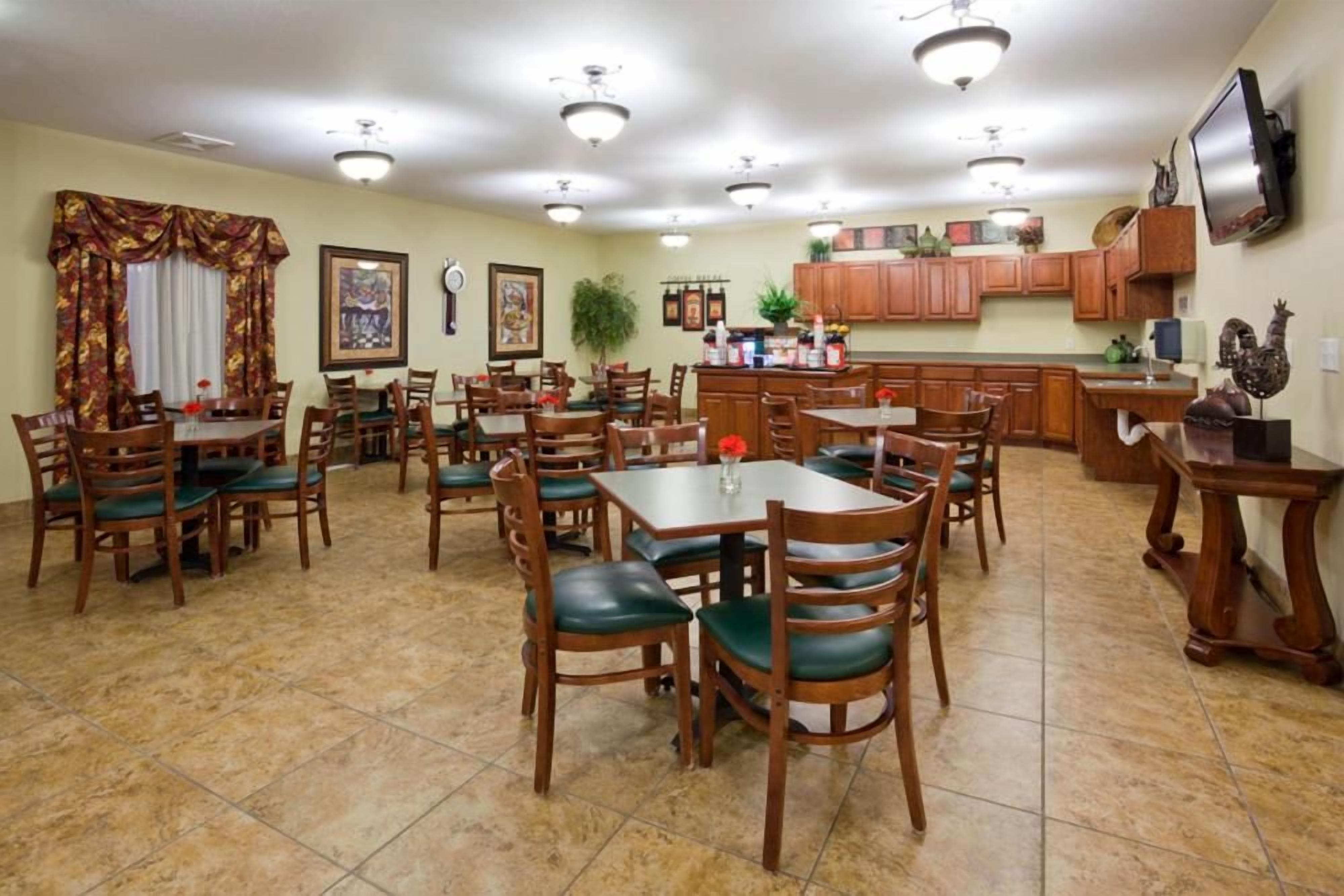 A dining area with multiple tables and chairs, a kitchen area with wooden cabinets, and a television mounted on the wall.