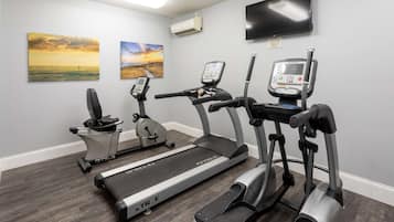 A home gym with treadmills, an elliptical, and a stationary bike, featuring a TV and artwork on the walls.