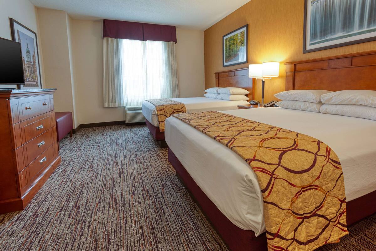 Ein Hotelzimmer mit zwei Betten, einem Schminktisch, einem Fernseher und einem Bild an der Wand.