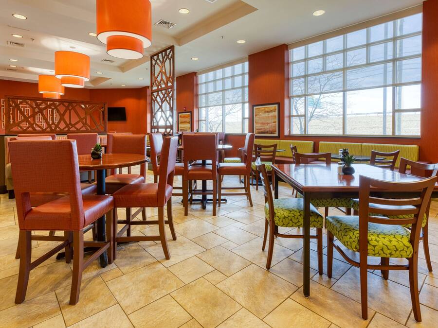 A dining area with multiple tables and chairs, large windows, and orange pendant lighting.