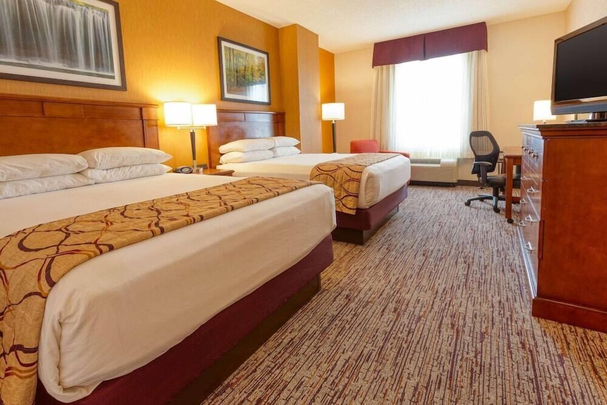 Ein Hotelzimmer mit zwei Betten, einem Fernseher, einem Schreibtisch und einem Fenster mit Vorhängen.