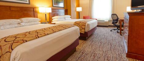 A hotel room with two beds, a desk, a television, and a large window with curtains.