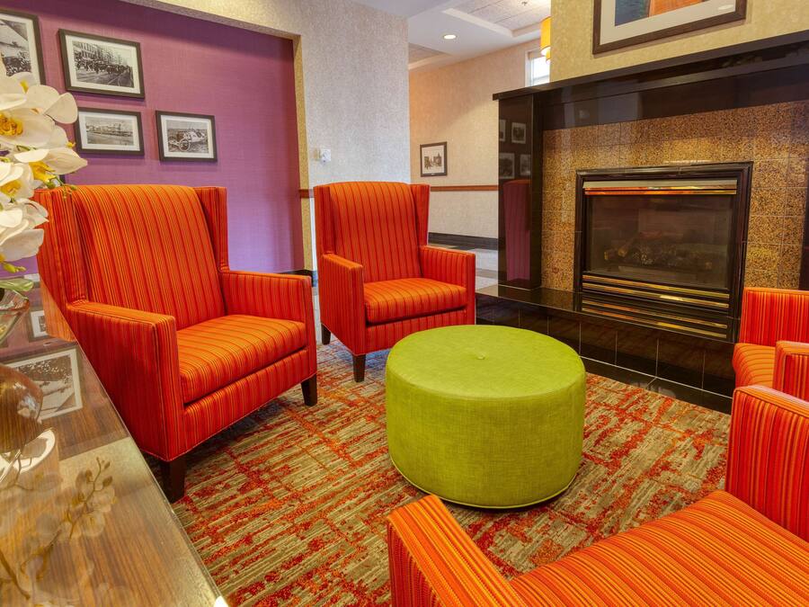 A room with red upholstered chairs, a green ottoman, and a fireplace.